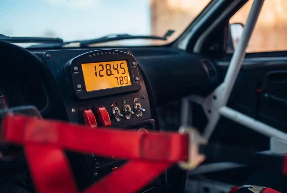 Rally tripmeter with an amber LCD readout, toggle switches, red harness in the foreground.